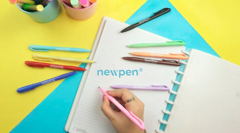 criança a escrever num caderno com canetas coloridas à volta