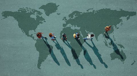 Grupo de jovens adultos a caminhar sobre mapa-mundo pintado no chão, representando mobilidade internacional 