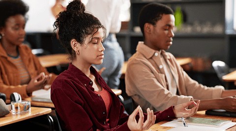 Estudantes adolescentes de olhos fechados a meditar na sala de aula