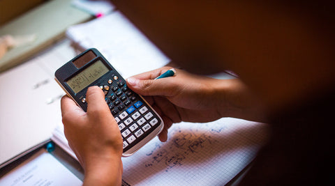 calculadora científica em primeiro plano sobre uma mesa de estudo, com livros e materiais escolares desfocados ao fundo