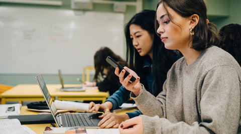 Estudantes a estudar com livros abertos enquanto utilizam um smartphone e um portátil com o uso do modo Estudo do ChatGPT como ferramenta inovadora de aprendizagem. 