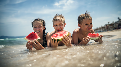 Crianças felizes a comer melancia na praia num dia de verão