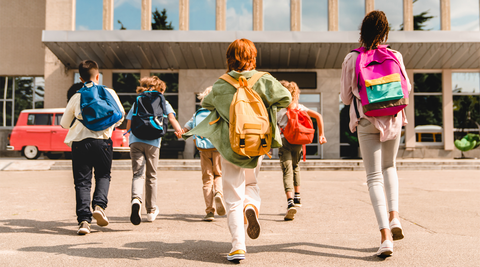 Grupo de crianças a correr para a escola com mochilas coloridas no primeiro dia de aulas