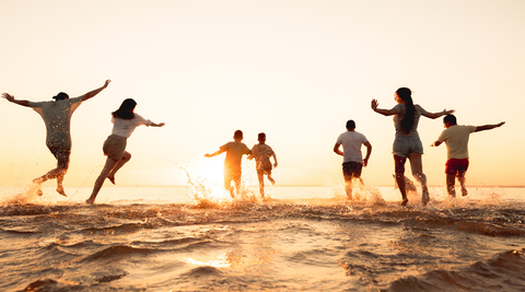 Grupo de crianças e adultos a correr e brincar no mar ao pôr do sol