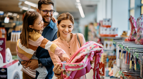 Menina feliz a apontar para a mochila escolar enquanto compra material escolar com os pais
