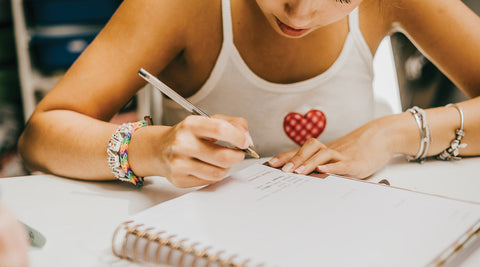 Estudante concentrada a escrever num caderno enquanto organiza o plano de estudo para os exames nacionais 