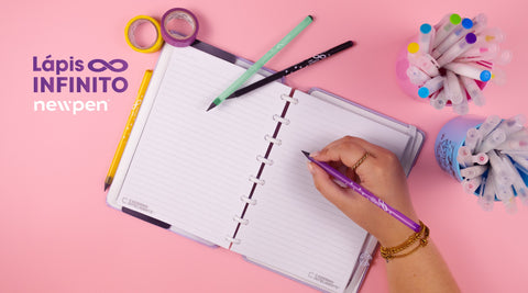 Mão a escrever com lápis inteligente num caderno e dois suportes com marcadores coloridos