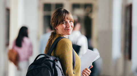 Aluna universitária sorridente com folhas de resumos nos braços e de mochila